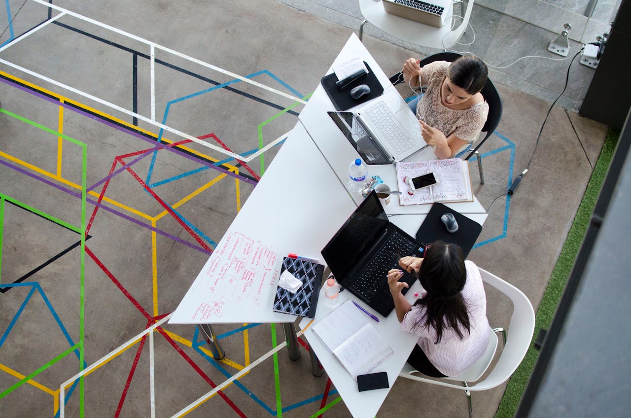 team-04 Overhead view of women working together in a modern office setting with colorful geometric floor design.